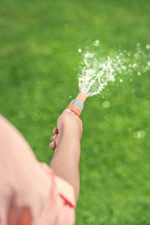 Gardener sprinkling water on green grass in a gardenの写真素材