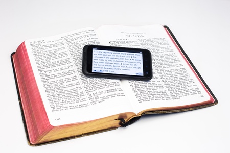 A smartphone rests on a worn Bible - both displaying the first verses of the the Gospel According to Johnl の写真素材