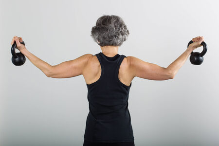 A smiling middle aged female sports trainer demonstrates the use of kettle bells. middle aged female sports trainer demonstrates the use of kettle bells.の写真素材