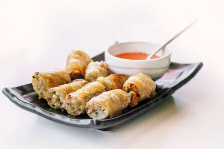 A plate of fried chinese spring rolls with chili sauce