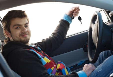 Happy young man sitting ina new car holding out keysの写真素材