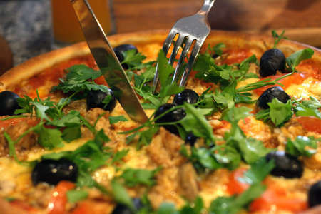 Macro shot of a fork and knife cutting a hot pizzaの写真素材