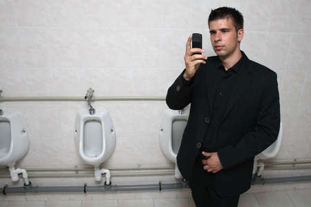 Businessman holding his mobile phone in a toilet, taking picture of himself.
の写真素材