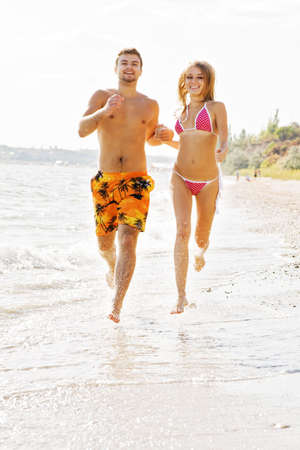 Young cheerful couple running along the beachの写真素材