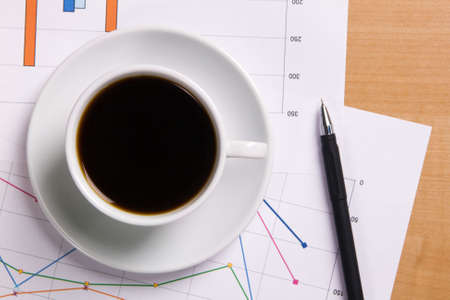 Cup of strong coffee over business diagrams, closeup soft focus photoの写真素材