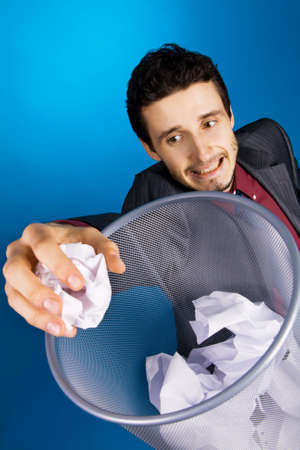 Young businessman playing baskteball with crumpled paper, blue backgroundの写真素材