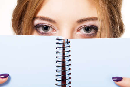 Lovely girl hiding behind notebook, white backgroundの写真素材