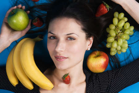 Closeup portrait of a beautiful young woman lying among fruitsの写真素材