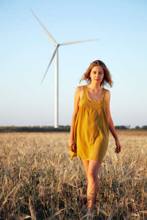 Lady walking in the field with wind power generator on backgroundの写真素材