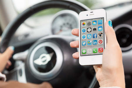 WROCLAW, POLAND - AUGUST 05, 2014: Photo of a young woman sitting in a Mini Cooper car holding an iPhone 4 smartphone device with main menu on screenのeditorial素材