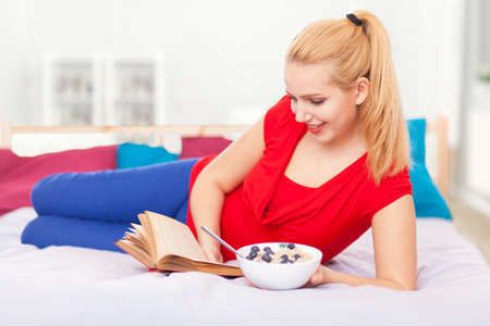 Young woman having breakfast and reading a book in bed.の写真素材