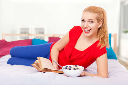 Young woman having breakfast and reading a book in bed.の写真素材