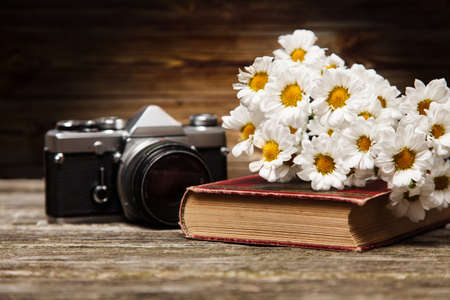 Photo camera, daisies and a book on a wooden backgroundの写真素材