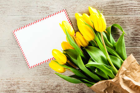 A Letter and yellow tulips on wooden background