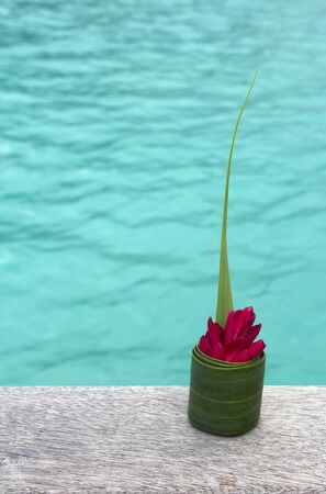 closeup of a flower wrapped in a palm leaf on a wooden pier by a lagoonの写真素材