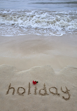 The word holiday written in the sand by the oceanの写真素材