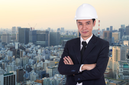 engineer in white helmet with arms crossed, city background