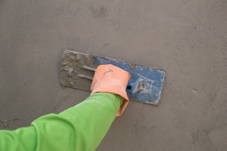 Close-up of hand using trowel to finish wet concrete wall at construction siteの写真素材