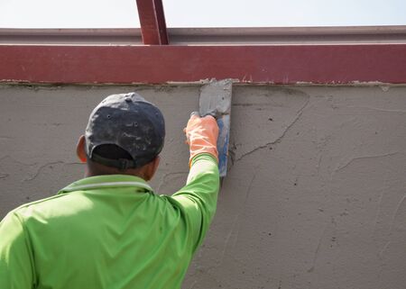 worker using trowel to finish wet concrete wall at construction siteの写真素材