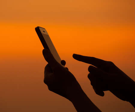 Silhouette of hand using mobile device at sunsetの写真素材