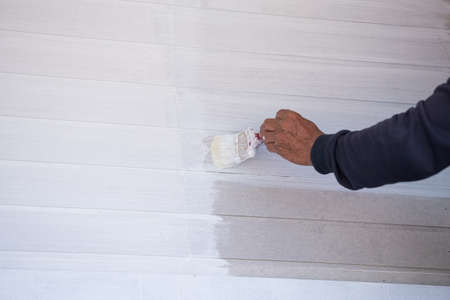 Hand holding brush painting the timber wall