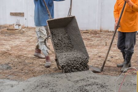 worker pouring cement from cart to floor at construction siteの写真素材