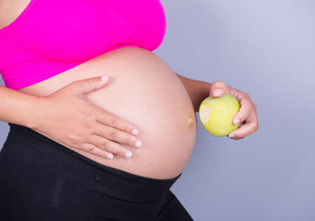 close-up belly of pregnant woman with green apple on gray wall backgroundの写真素材