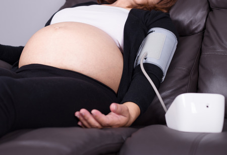 Pregnant woman measures blood pressure with automatic sphygmomanometer