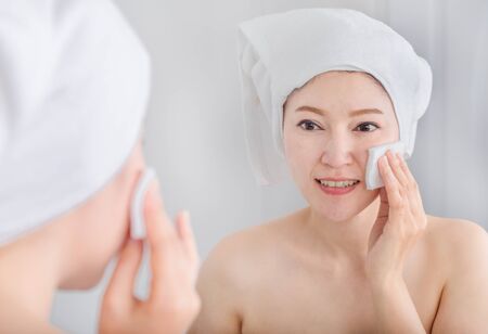 Beautiful woman looking mirror and cleaning her face with cottonの写真素材