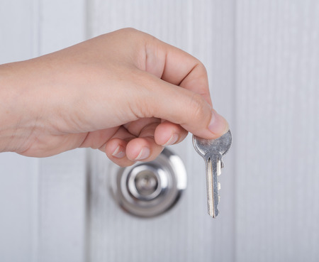 key in hand with door knob and white door background