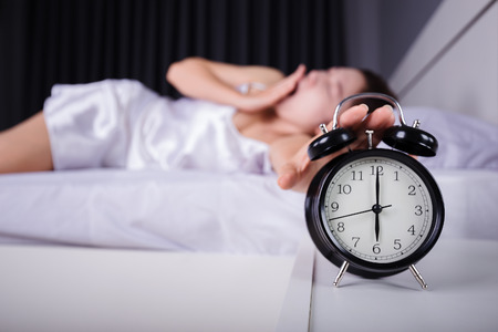 woman sleeping and wake up to turn off the alarm clock in the morningの写真素材