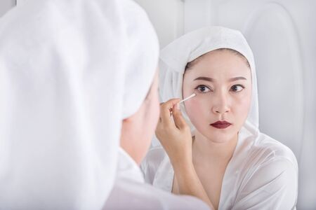 Beautiful woman looking mirror and remove makeup beside eye with a cotton swabの写真素材