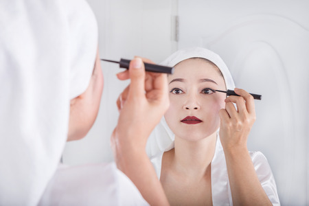 Beautiful woman looking mirror and make-up with black eyelinerの写真素材