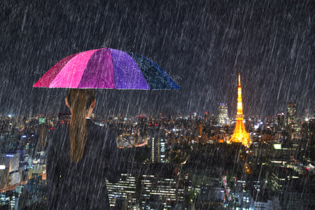 business woman holding multicolored umbrella with falling rain at tokyo city background, Japanの写真素材