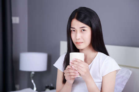 woman on bed with a cup of coffee in the bedroomの写真素材