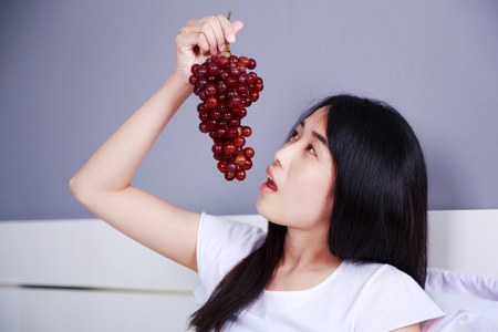 woman with red grape on bed in the bedroomの写真素材