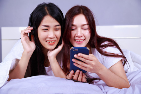 two woman using a phone in her hand on bed in the bedroomの写真素材