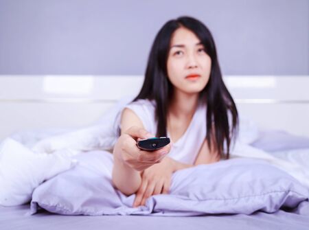 woman watching tv with remote on bed in the bedroom