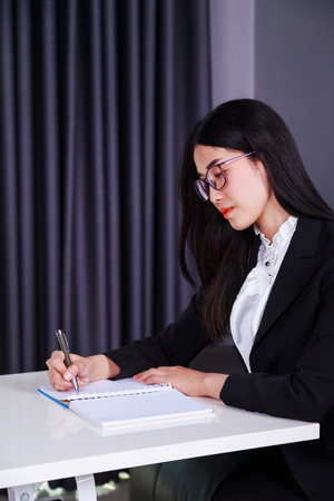 young business woman sitting at the desk and writes a note on the notebookの写真素材