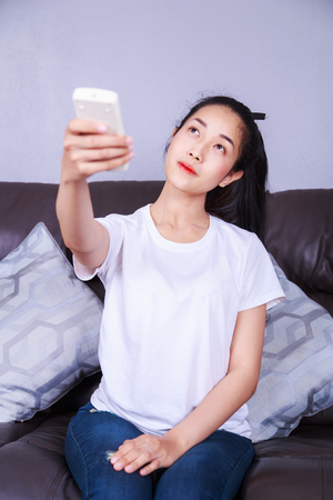 young woman holding a remote control air conditioner on sofa at homeの写真素材