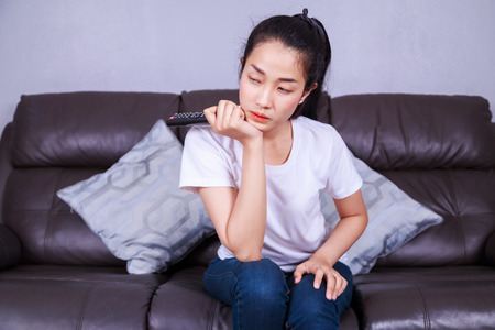 woman with tv remote control on sofa in living room at homeの写真素材