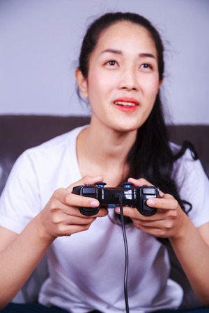 woman using joystick controller playing video game on sofa in living room at homeの写真素材