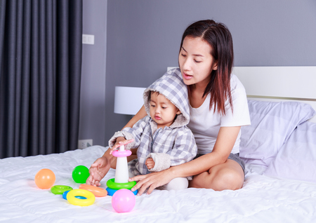 baby playing toys with mother on bed at homeの写真素材