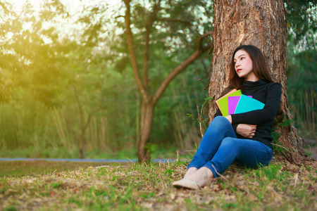young woman sitting and holding a book in the parkの写真素材
