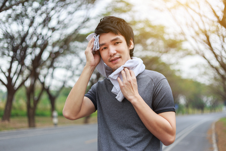 young sporty man resting and wiping his sweat with a towel after workout sport exercises outdoors at the parkの写真素材