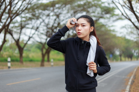 young sporty woman running and wiping her sweat with a towel in the parkの写真素材