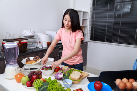 young woman mixing salad while cooking in kitchen の写真素材