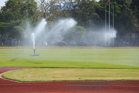 Sprinklers spraying water on grass in football fieldの写真素材
