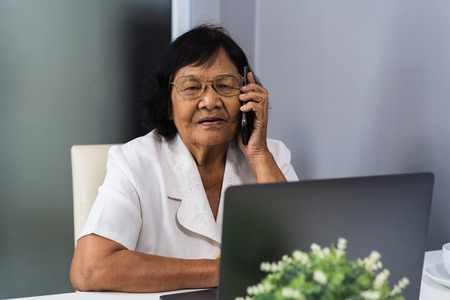senior woman talking on mobile phone and using laptop computerの写真素材