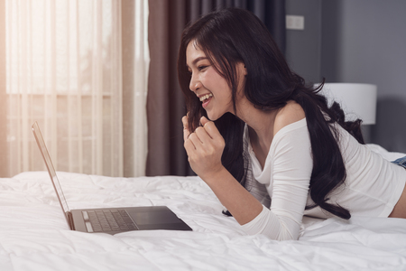 surprised woman using a laptop computer on bedの写真素材